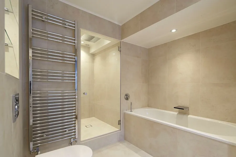 Step-up wet room beside a bath with a chrome towel rail