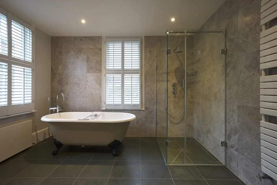 Roll-top bath with stone walls and a frameless shower