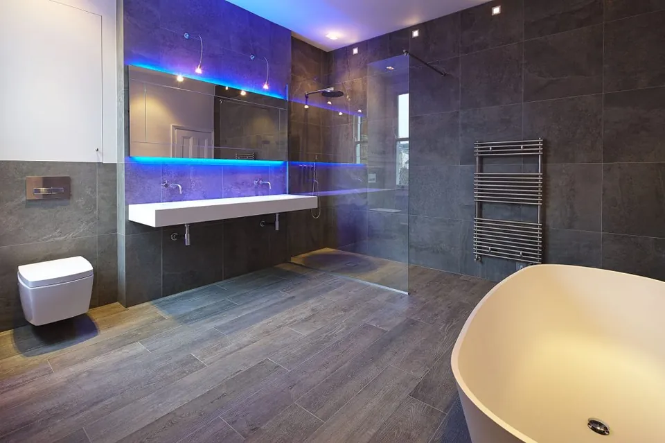 Dark-tiled wet room with a freestanding bath and LED shelving
