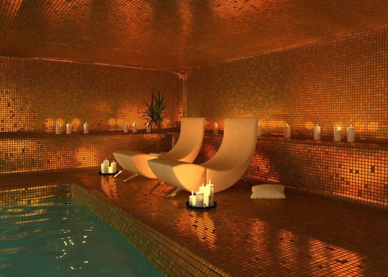 A gold mosaic pool lit by candlelight with two loungers