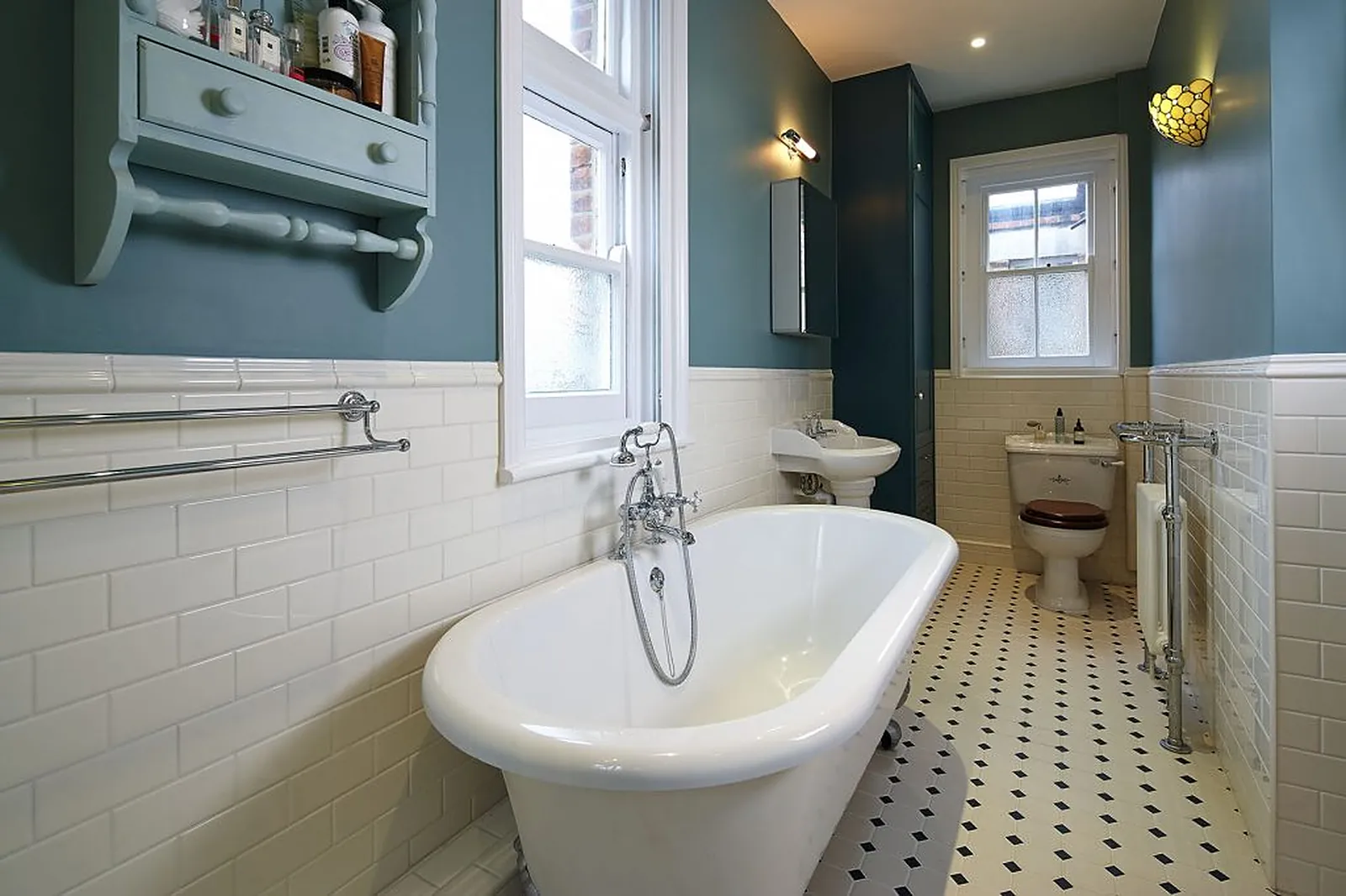 A teal-walled bathroom with a freestanding roll-top bath and metro tiles