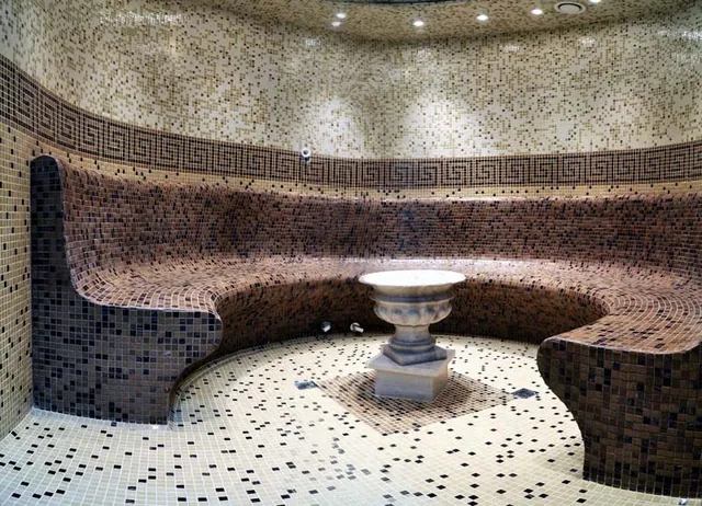 A mosaic hammam with curved heated seating around a fountain